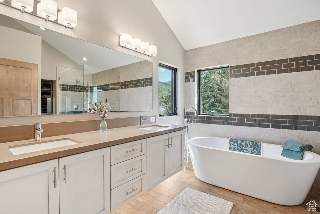 Full bath with vaulted ceiling, double vanity, a shower stall, a freestanding tub, and wood finished floors