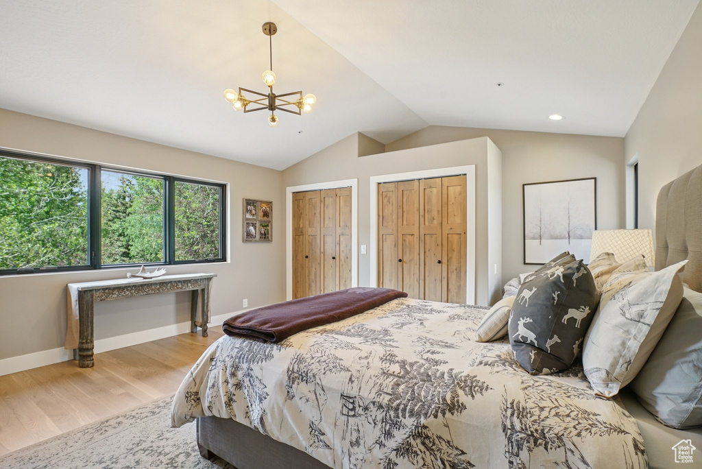 Bedroom featuring two closets, vaulted ceiling, a chandelier, and wood finished floors
