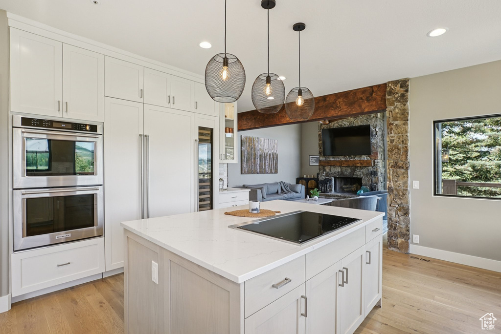 Kitchen featuring double oven, black electric stovetop, white cabinetry, and recessed lighting