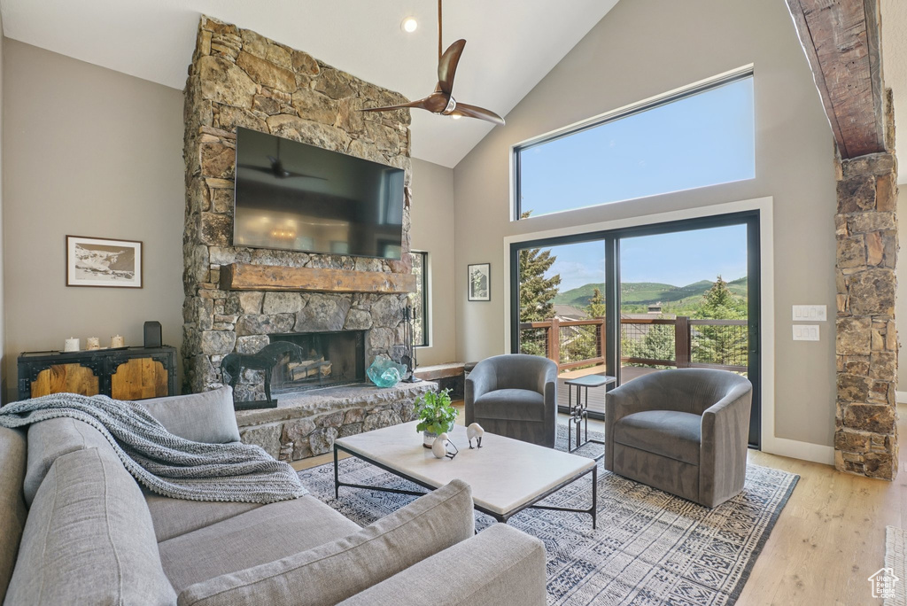 Living room with a ceiling fan, a stone fireplace, high vaulted ceiling, and wood finished floors