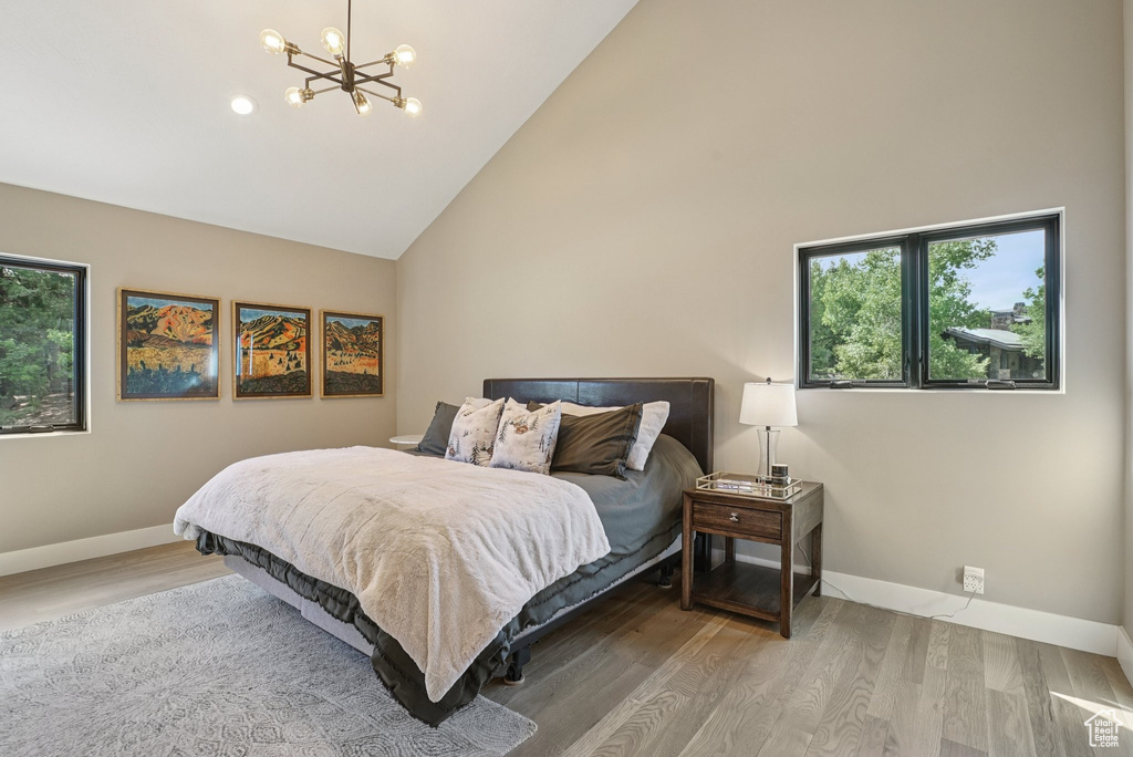 Bedroom with high vaulted ceiling, multiple windows, a chandelier, and wood finished floors