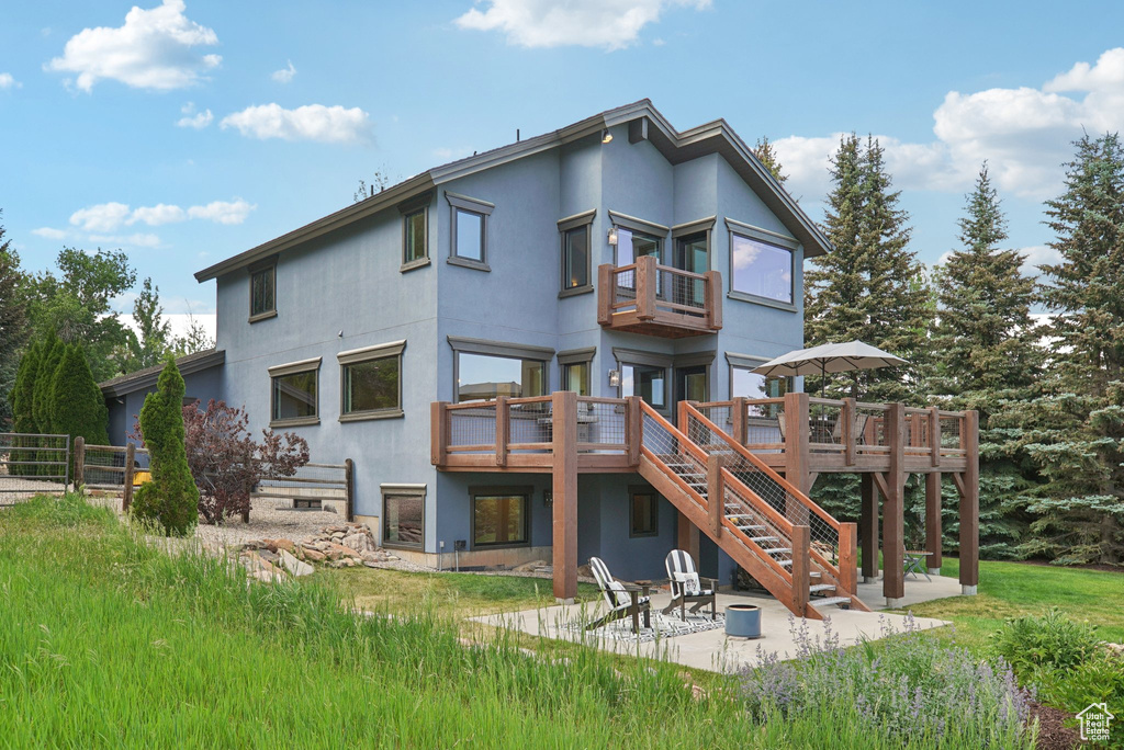 Rear view of house featuring stucco siding, stairs, a balcony, and a patio area