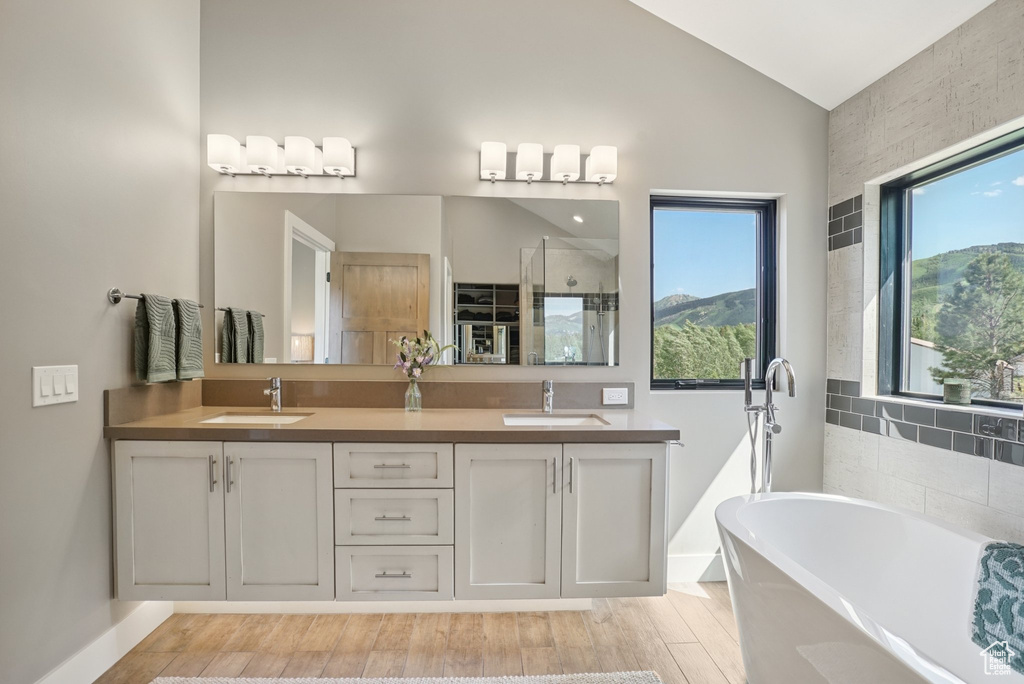 Bathroom with a freestanding tub, lofted ceiling, double vanity, a stall shower, and wood finished floors