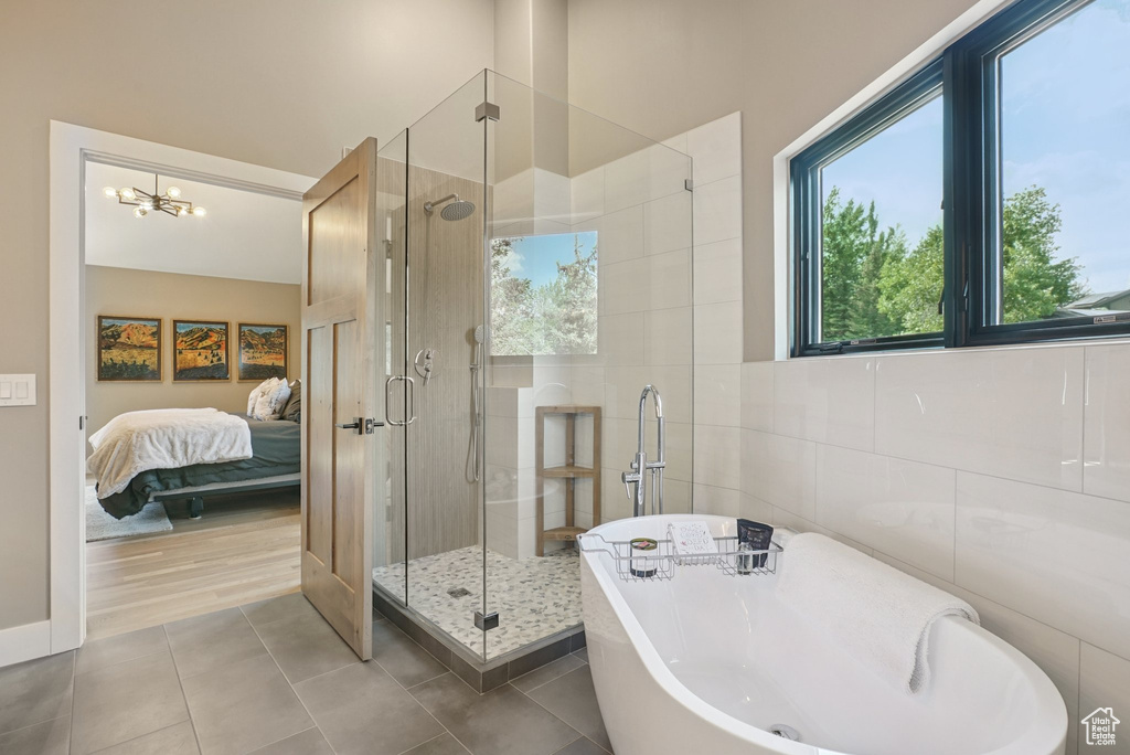 Ensuite bathroom featuring tile walls, a soaking tub, a stall shower, tile patterned floors, and a chandelier