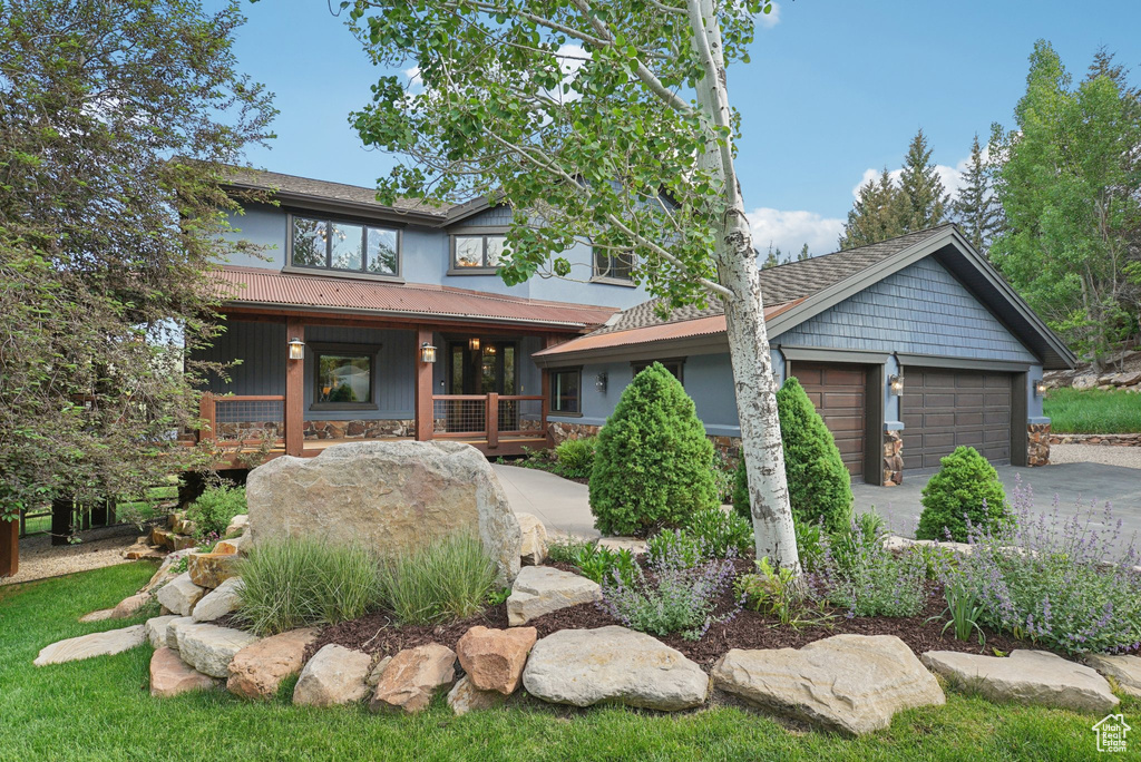 View of front of property featuring a porch, concrete driveway, stone siding, and a garage