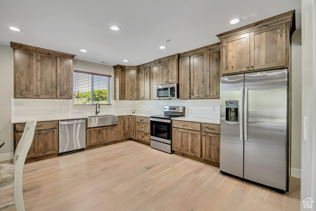 Kitchen featuring stainless steel appliances, light wood-style floors, backsplash, recessed lighting, and light countertops