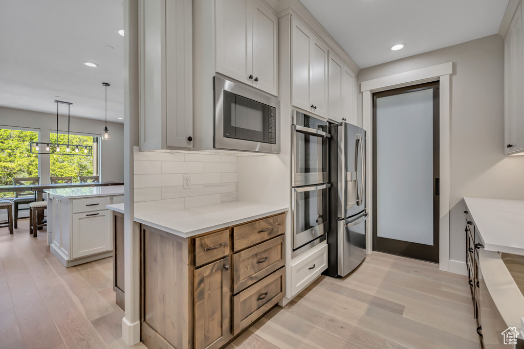 Kitchen with stainless steel appliances, light wood-type flooring, tasteful backsplash, light countertops, and recessed lighting