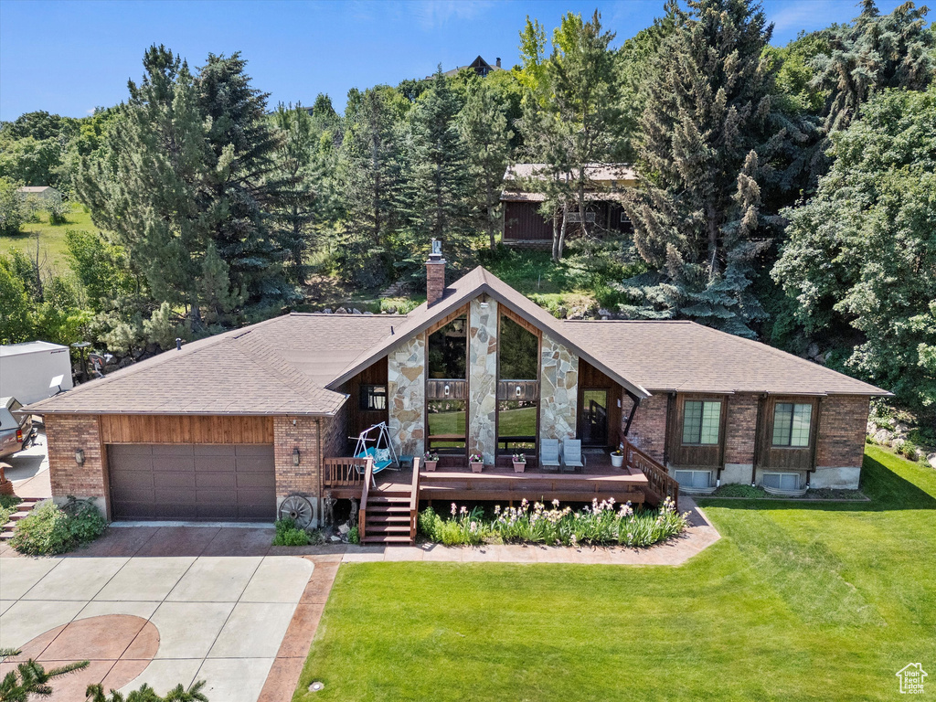 View of front of property featuring brick siding, driveway, a front yard, a chimney, and an attached garage