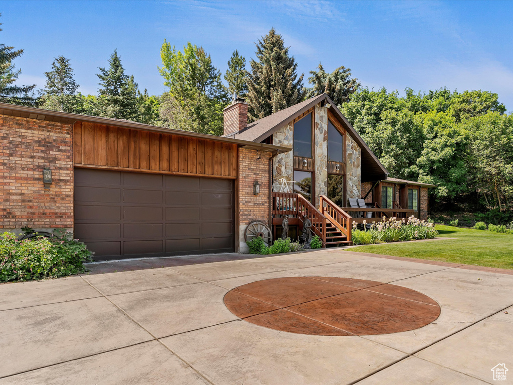 View of front of home with brick siding, a chimney, concrete driveway, an attached garage, and a front yard