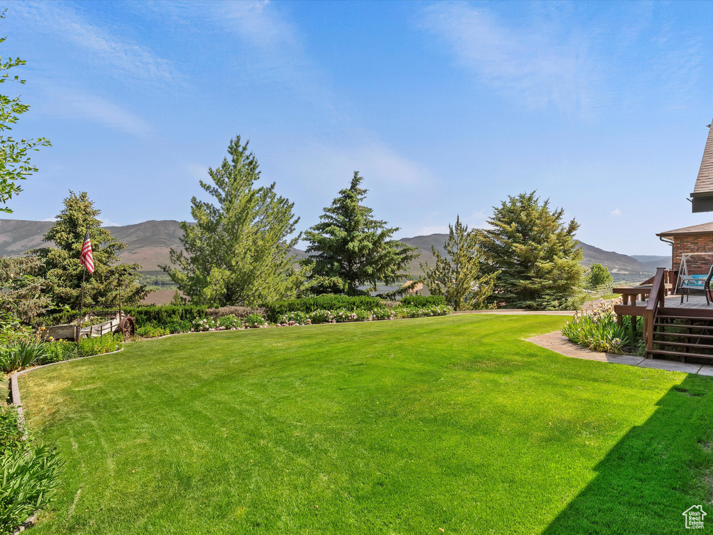 View of grassy yard with a deck with mountain view