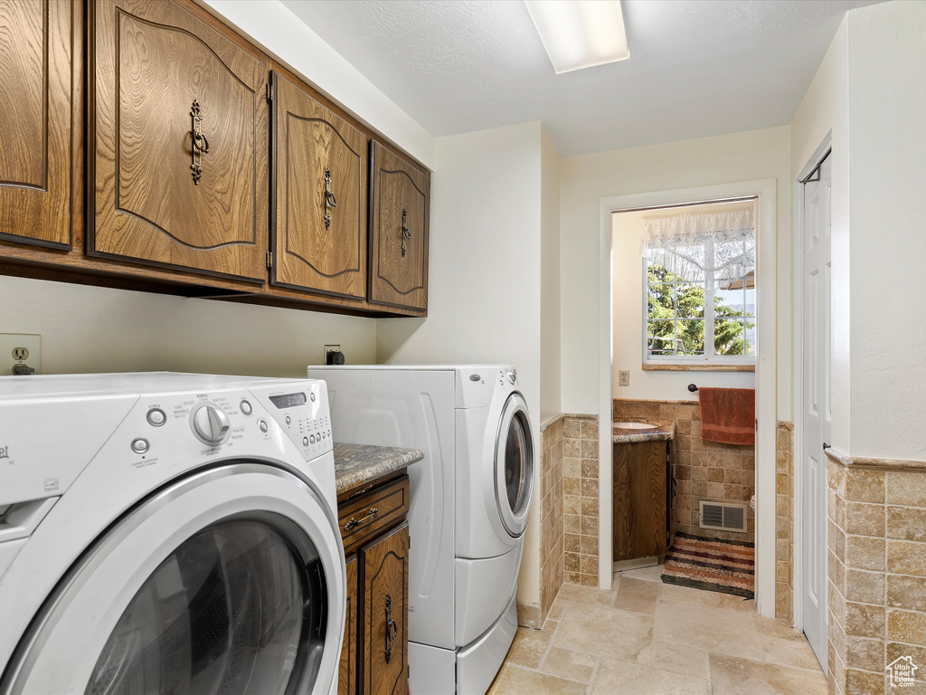 Laundry room featuring tile walls, cabinet space, independent washer and dryer, and a wainscoted wall