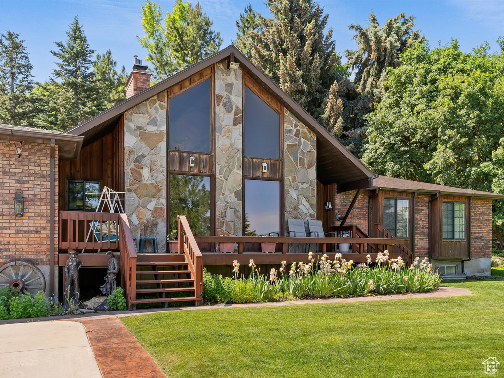 View of front of home featuring a front yard, a chimney, a deck, stone siding, and brick siding