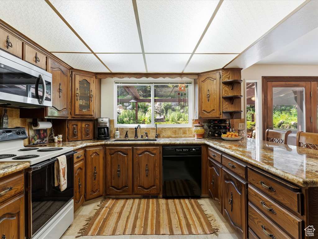 Kitchen with white range with electric cooktop, black dishwasher, stainless steel microwave, open shelves, and a peninsula