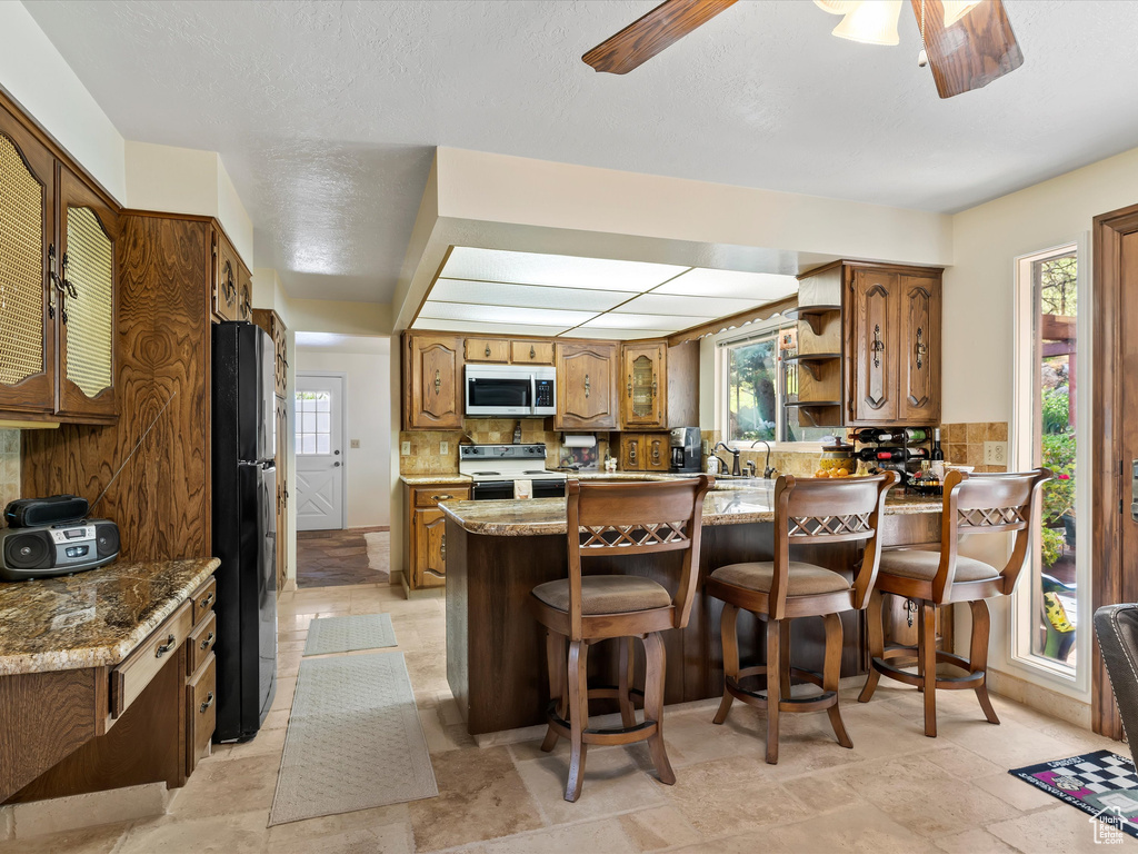 Kitchen featuring stainless steel microwave, freestanding refrigerator, white range with electric stovetop, a peninsula, and a ceiling fan
