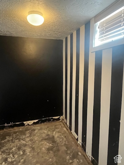 Spare room with wallpapered walls, a textured ceiling, and concrete floors