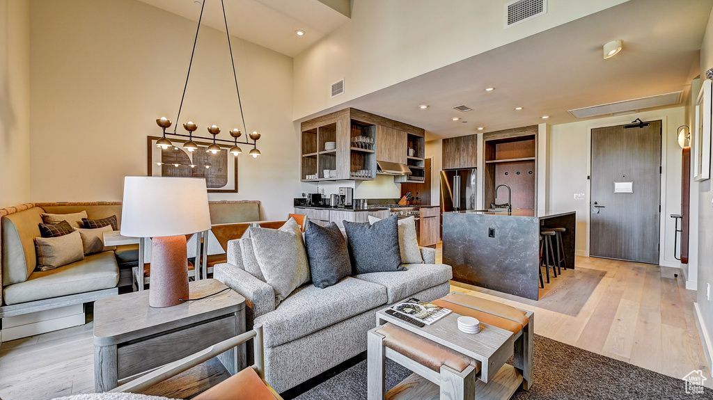 Living area with light wood-style floors, a towering ceiling, and a chandelier