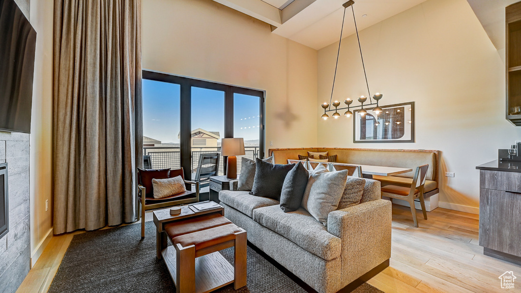 Living area featuring a towering ceiling, light wood-type flooring, a glass covered fireplace, and a chandelier