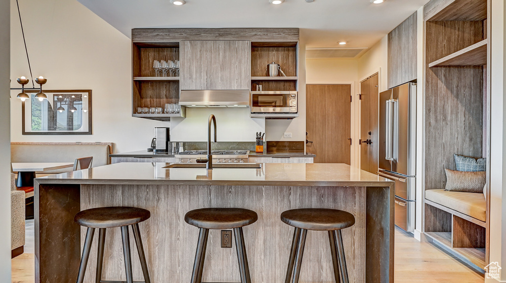 Kitchen featuring open shelves, appliances with stainless steel finishes, modern cabinets, a breakfast bar area, and light wood finished floors