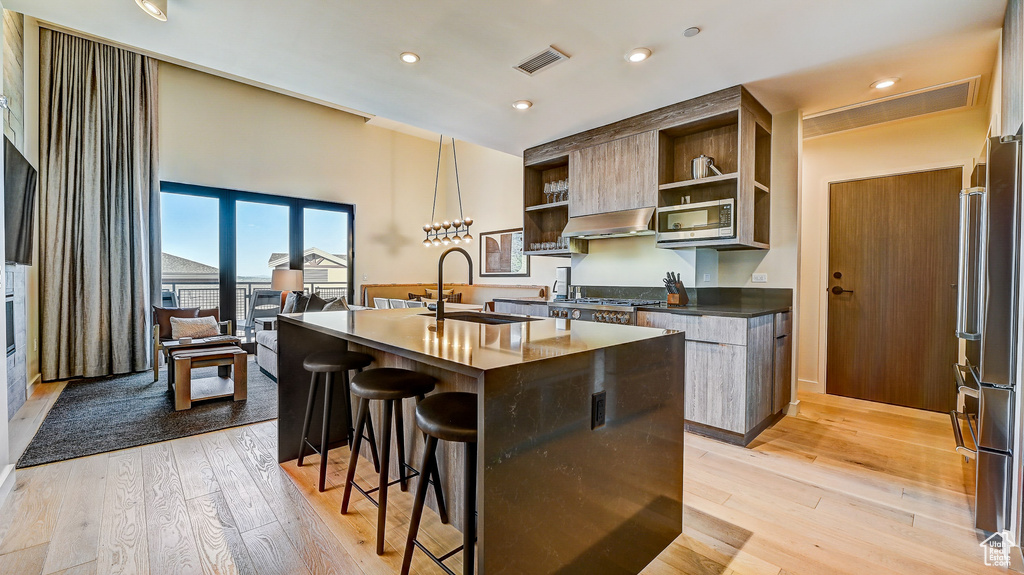 Kitchen with open shelves, stainless steel appliances, under cabinet range hood, a breakfast bar, and dark countertops