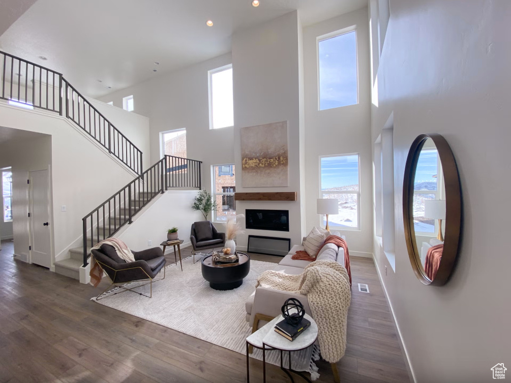 Living room with a high ceiling, stairway, wood finished floors, recessed lighting, and a glass covered fireplace