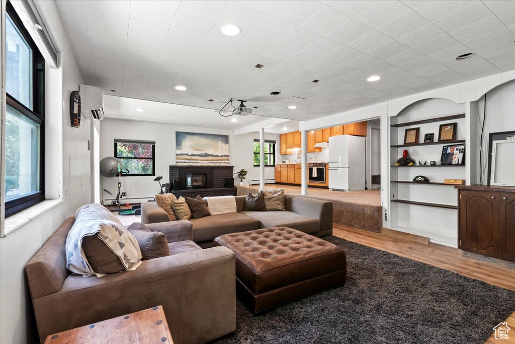 Living room featuring light wood finished floors, an AC wall unit, a brick fireplace, and recessed lighting