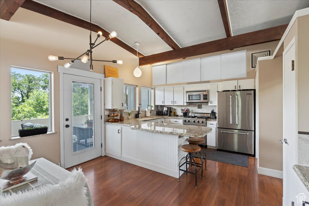 Kitchen with high end appliances, a peninsula, decorative backsplash, a chandelier, and beam ceiling