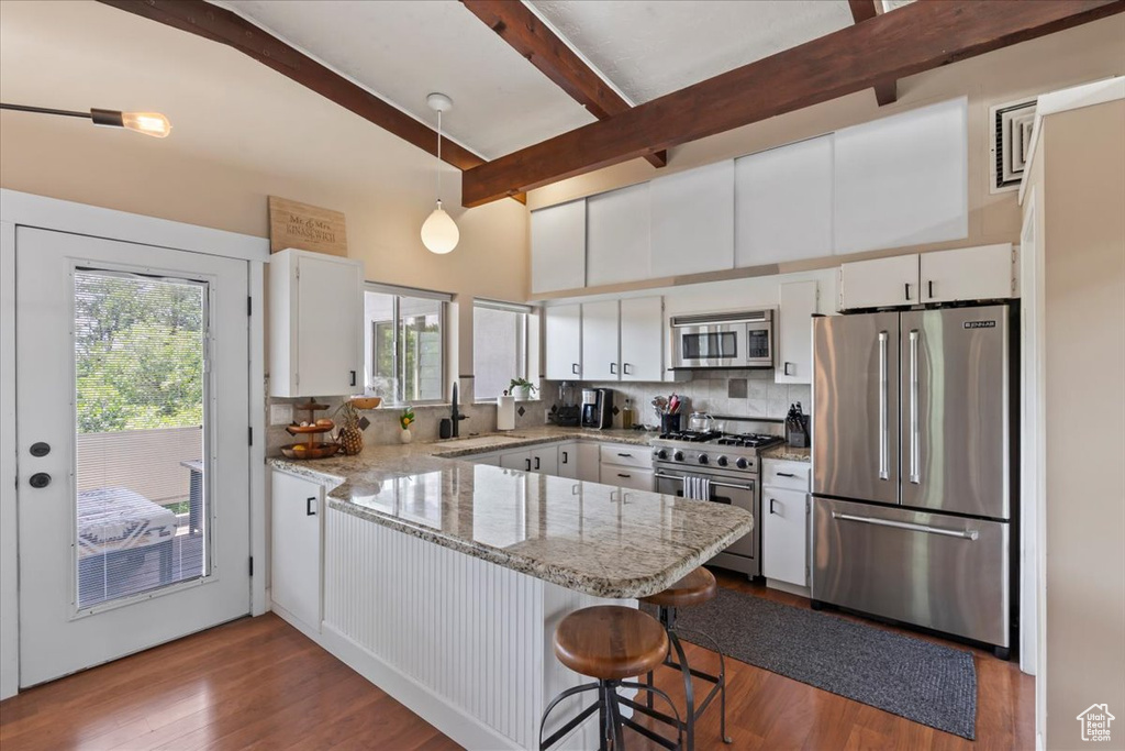Kitchen featuring high quality appliances, a peninsula, backsplash, white cabinets, and dark wood finished floors