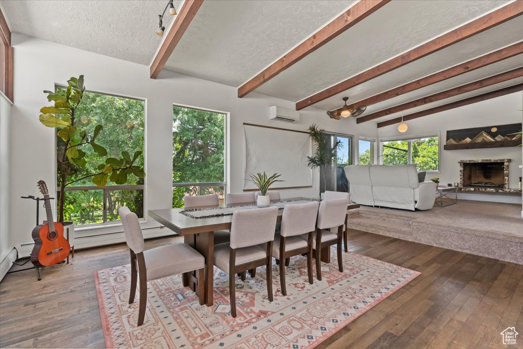 Dining space with a wall unit AC, beam ceiling, dark wood-style flooring, a fireplace with raised hearth, and a textured ceiling