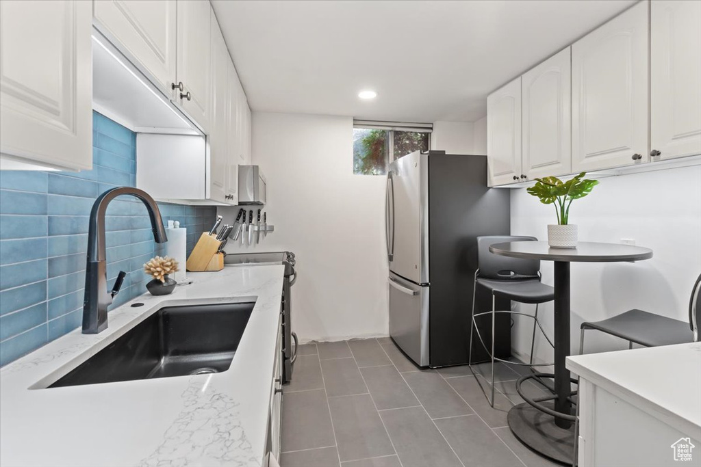 Kitchen featuring freestanding refrigerator, white cabinets, tasteful backsplash, tile patterned flooring, and recessed lighting