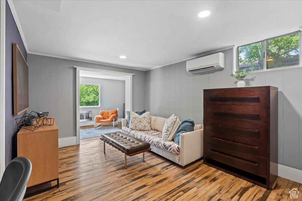 Living area featuring a wall mounted air conditioner, healthy amount of natural light, ornamental molding, light wood-type flooring, and a decorative wall