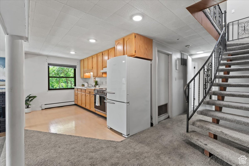 Kitchen with freestanding refrigerator, light carpet, stainless steel stove, baseboard heating, and light countertops