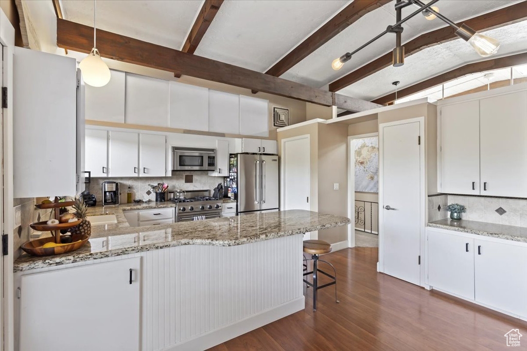 Kitchen with high end appliances, a peninsula, tasteful backsplash, dark wood-style floors, and hanging light fixtures