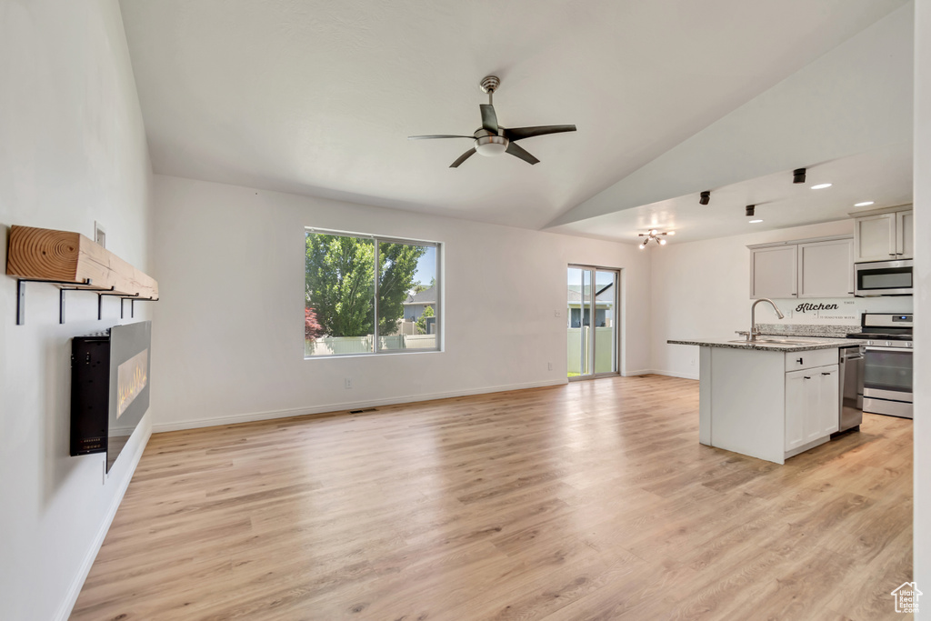Unfurnished living room with a ceiling fan, lofted ceiling, light wood-style flooring, and a glass covered fireplace