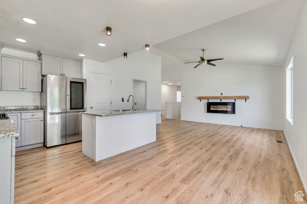 Kitchen with smart refrigerator, light wood finished floors, lofted ceiling, ceiling fan, and a glass covered fireplace