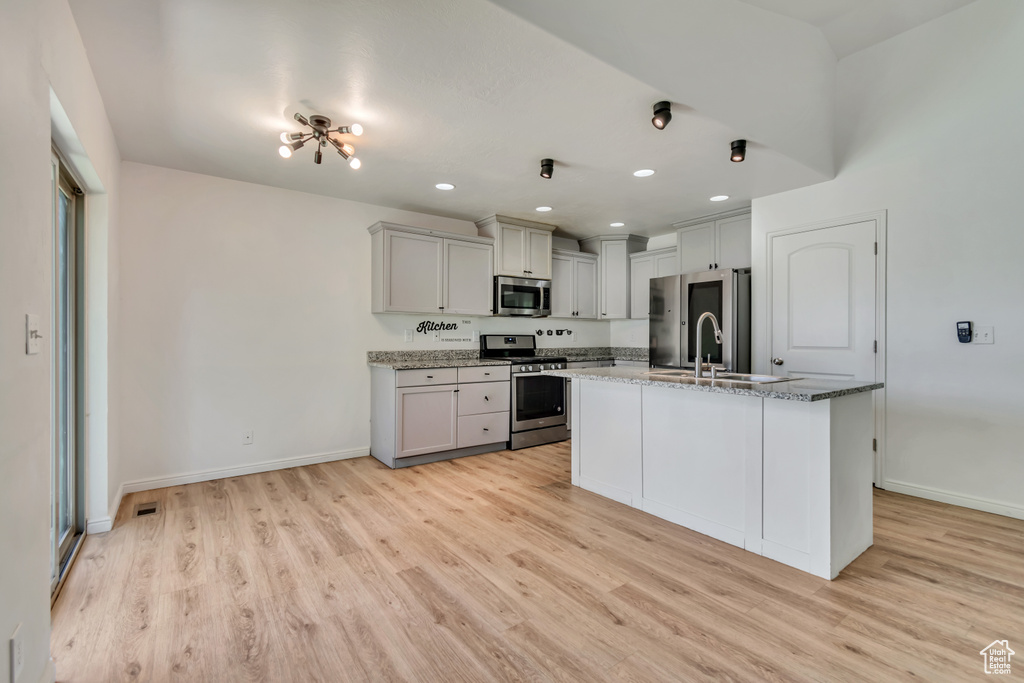 Kitchen featuring appliances with stainless steel finishes, light wood finished floors, light stone countertops, a kitchen island with sink, and recessed lighting