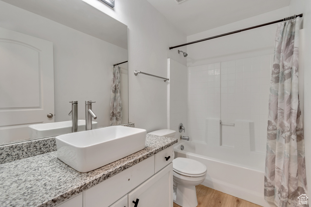 Full bath with shower / bath combo with shower curtain, vanity, and wood finished floors