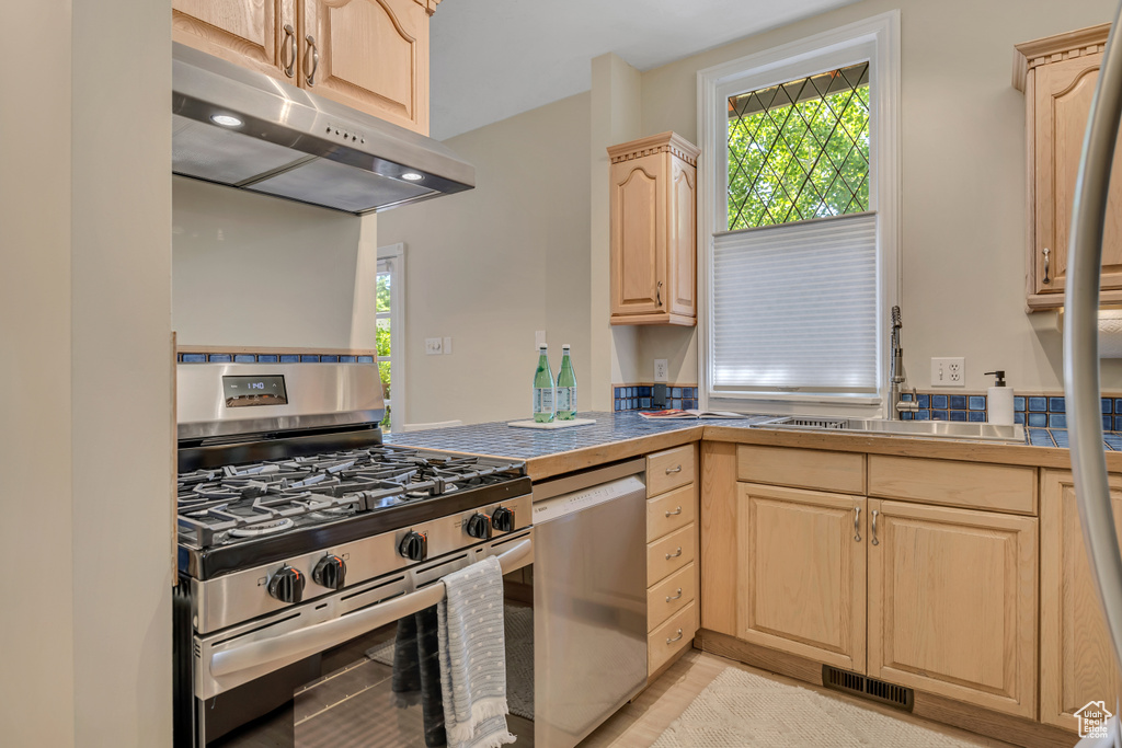 Kitchen featuring stainless steel appliances, under cabinet range hood, and light brown cabinets