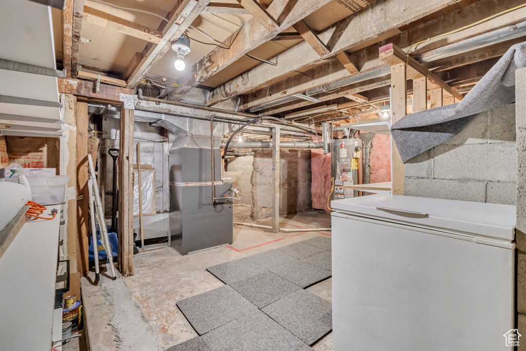 Unfinished basement with white fridge, gas water heater, and heating unit