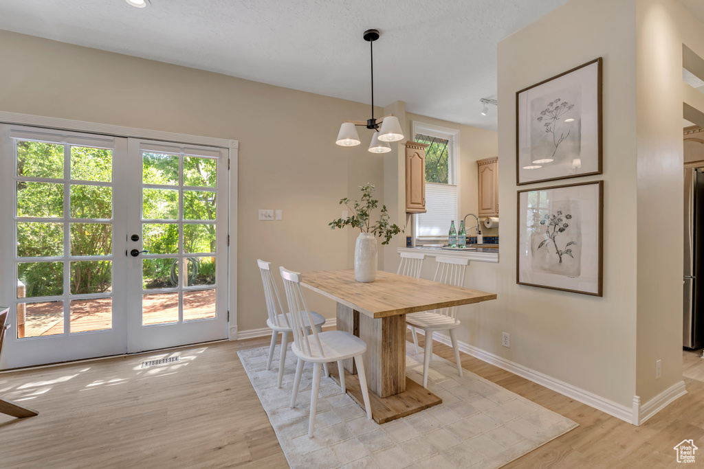 Dining area with light wood finished floors, french doors, and a chandelier