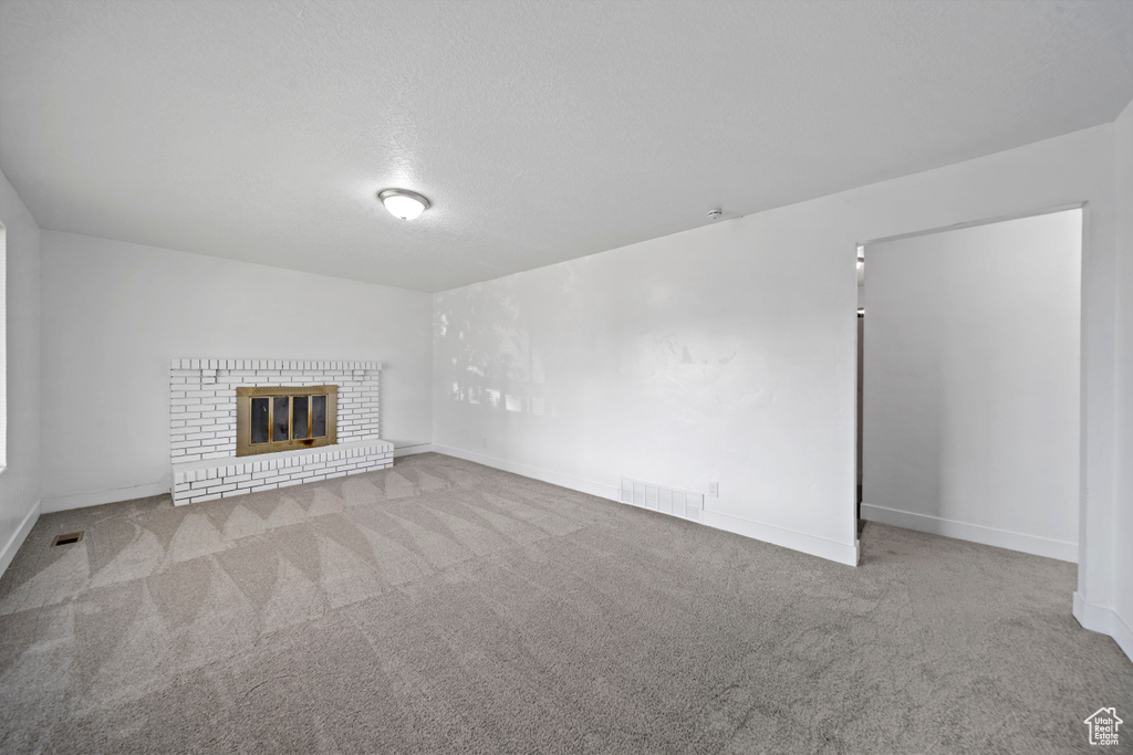 Unfurnished living room featuring carpet floors, a brick fireplace, and a textured ceiling