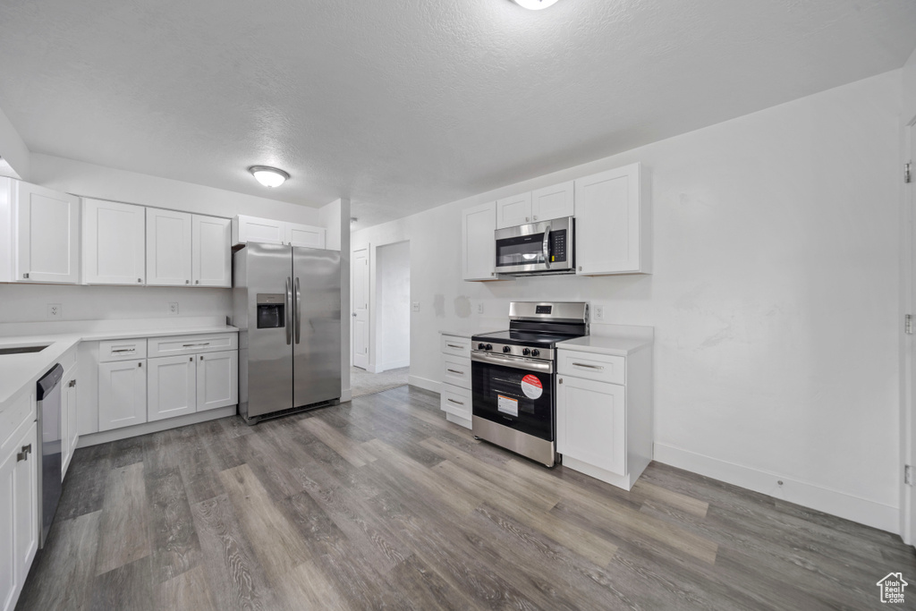 Kitchen with appliances with stainless steel finishes, light countertops, wood finished floors, white cabinets, and a textured ceiling