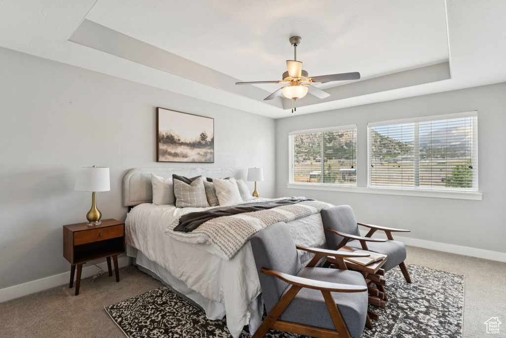 Carpeted bedroom with a raised ceiling and ceiling fan