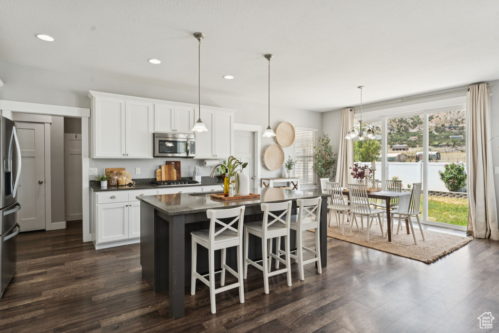 Kitchen with stainless steel appliances, white cabinets, a center island with sink, dark wood-type flooring, and recessed lighting