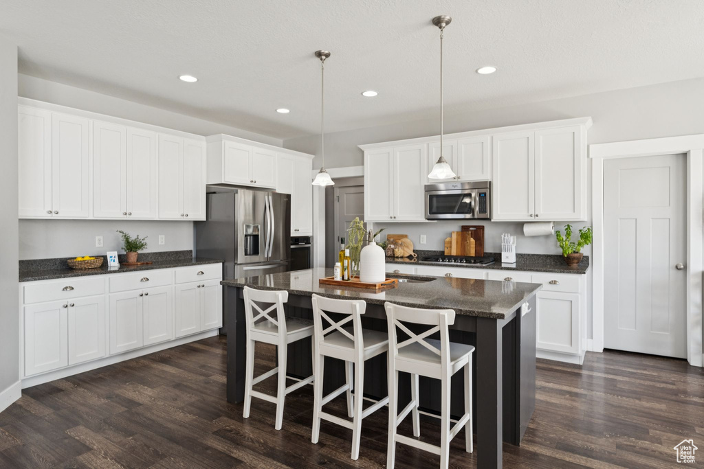 Kitchen with appliances with stainless steel finishes, recessed lighting, an island with sink, dark wood finished floors, and white cabinets