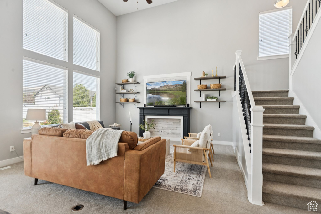 Carpeted living room featuring stairway, a ceiling fan, and a high ceiling