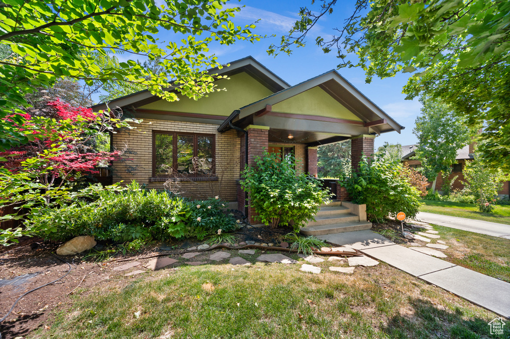 View of front of home featuring covered porch, brick siding, and a front yard