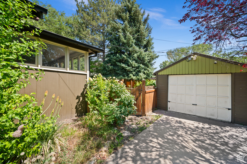 View of property exterior with concrete driveway, a garage, an outdoor structure, and a sunroom
