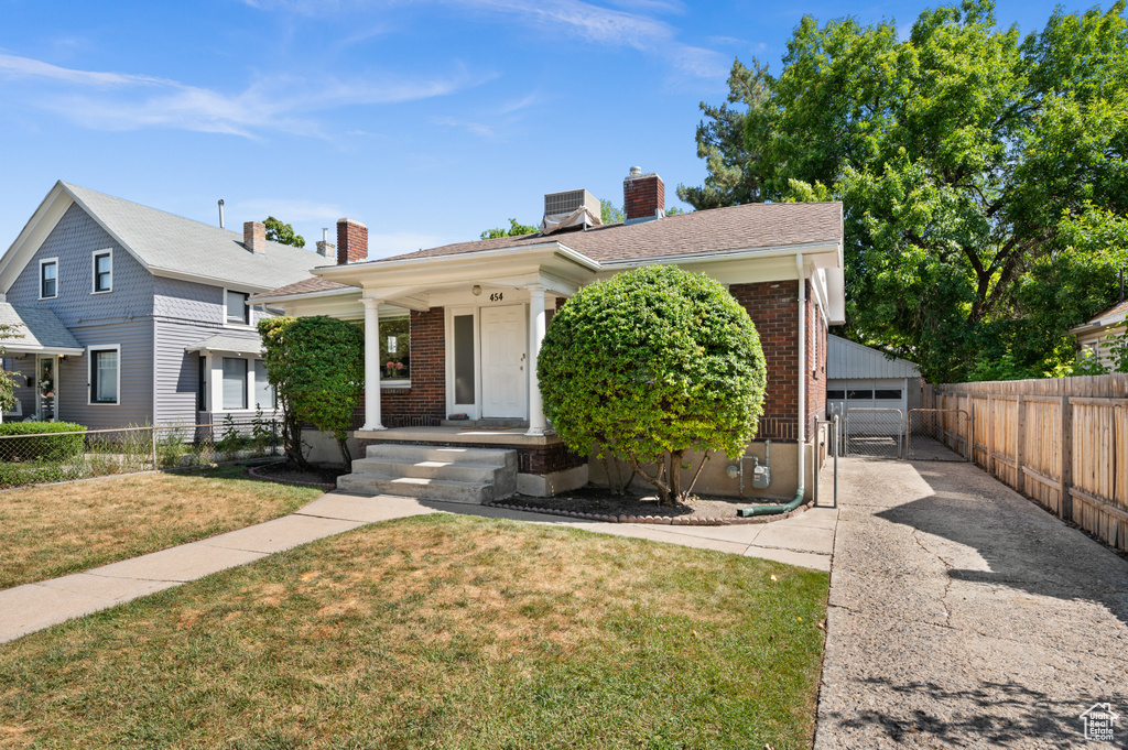 View of front of house featuring a chimney, brick siding, an outdoor structure, a detached garage, and covered porch