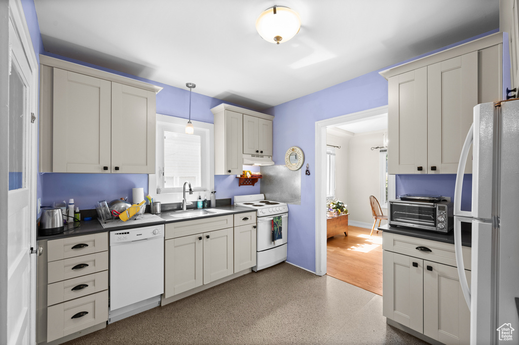 Kitchen featuring white appliances, dark countertops, under cabinet range hood, and decorative light fixtures
