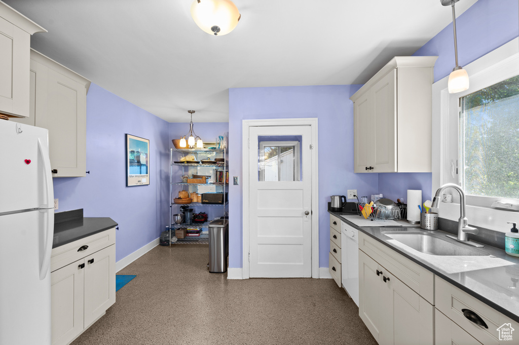 Kitchen with freestanding refrigerator, decorative light fixtures, dark countertops, and white cabinetry